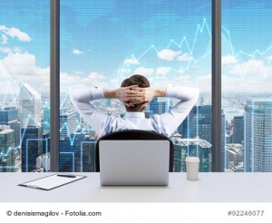 Rear view of the relaxing businessman with crossed hands behind his head, who is looking at NYC. Modern Panoramic office or work place with New York city view. Financial charts are over the windows.